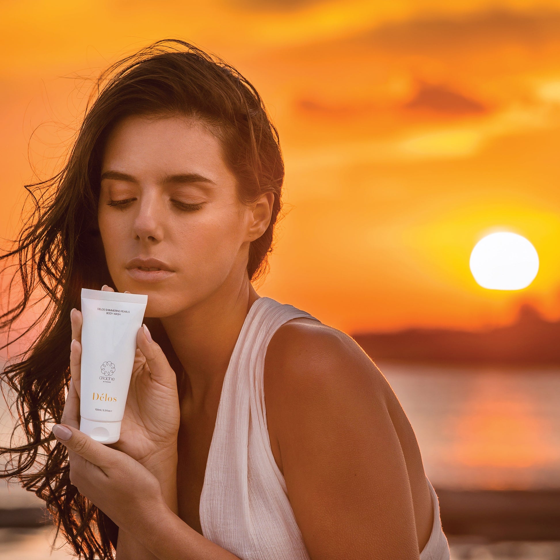 A woman holds the Délos Shimmering Pearls Body Wash during sunset.